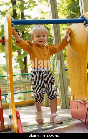 Ein schönes, fröhliches kleines Mädchen auf einer Kinderrutsche im Park. Haben Sie ein schönes Wochenende mit Ihrer Familie. Lifestyle Stockfoto