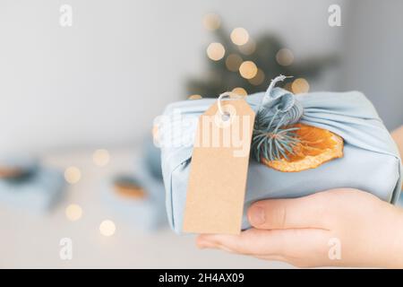 Dekoratives Weihnachtsgeschenk in umweltfreundlichem, wiederverwendbarem Stoffpaket mit Anhänger und Öko-Dekor auf einem Hintergrund von Girlanden Stockfoto