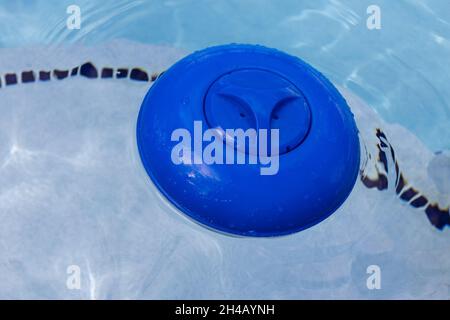 Blauer Chlorspender aus Kunststoff, der auf der Wasseroberfläche in einem Schwimmbad schwimmt. Stockfoto