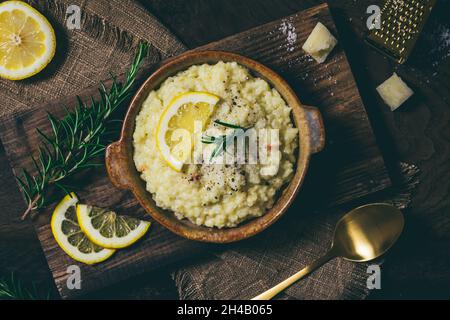 Zitronenreis-Risotto mit Rosmarin und frischen Zitronenscheiben auf dunklem Holzhintergrund, Draufsicht Stockfoto