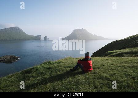 Der Wanderer genießt die wunderschöne Natur der Färöer-Inseln. Der Blick auf den Drangarnir von der malerischen Straße zwischen Bour und Gaadalur Stockfoto