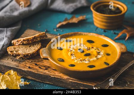 Kürbissuppe mit Creme und Samen auf einem rustikalen Holzbrett auf blauem Hintergrund Stockfoto
