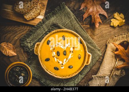 Kürbissuppe mit Creme und Samen auf rustikalem Metall- und Holzhintergrund mit Herbstblättern, Draufsicht Stockfoto