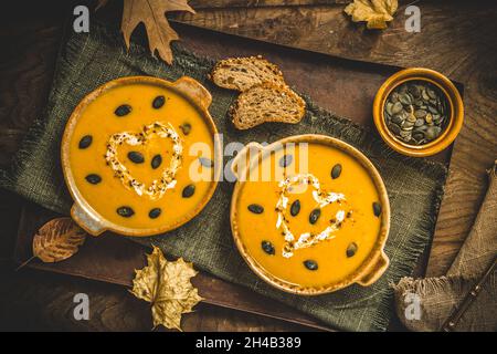 Kürbissuppe mit Creme und Samen auf rustikalem Metall- und Holzhintergrund mit Herbstblättern, Draufsicht Stockfoto
