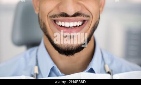 Ergebnis Der Zahnbehandlung. Nahaufnahme des glücklichen jungen arabischen Mannes, der mit seinen perfekten weißen Zähnen weithin lächelt, während er am Dentist Chair nach Check U sitzt Stockfoto