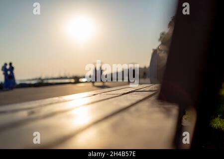 Sitzbank aus Holz im Park und Silhouetten von Menschen mit Sonnenlicht Stockfoto