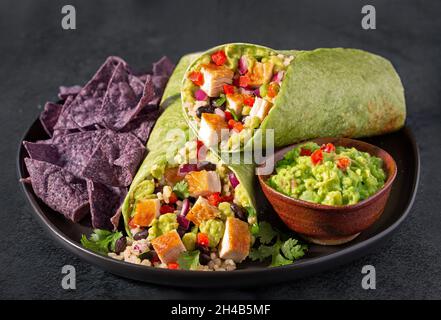 Huhn und Burrito aus schwarzen Bohnen in einer Spinatpackung mit blauen Mais-Tortilla-Chips und Guacomole Stockfoto