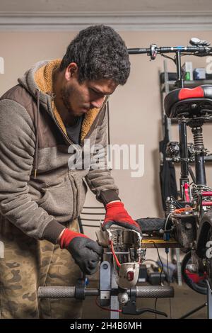 Vertikales Bild eines Mechanikers, der einen Kotflügel eines Elektrorollers auf einem Tisch in der Werkstatt repariert. Stockfoto