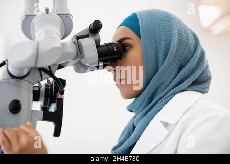 Junge Weibliche Zahnärztin In Hijab Arbeitet Mit Modernen Zahnmedizinischen Mikroskop In Der Klinik, Muslimische Stomatologin Frau Mit Professionellen Medizinischen Geräten Stockfoto