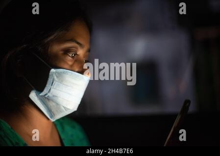 Frau in Maske, die ihr Handy in einem Auto sitzend ansieht Stockfoto