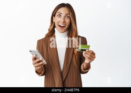 Online-Shopping. Staunende Frau mittleren Alters mit Kreditkarte und Handy-App, lächeln aufgeregt von Anwendung zu bestellen smth, weißen Hintergrund Stockfoto
