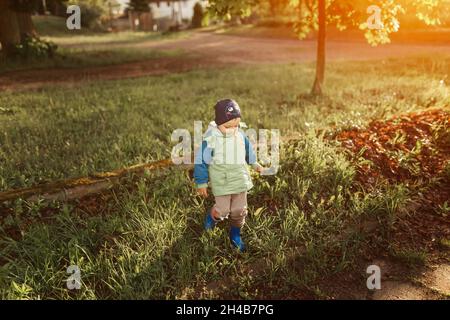 Kleiner Junge, der mit blauen Wellingtons auf Gras im Park läuft Stockfoto