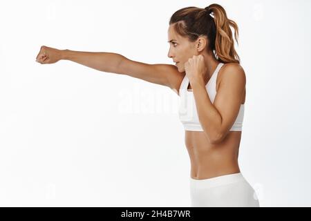 Weibliche Kämpferin, Luft schlagen, Kampfübungen, Schattenboxen im Fitnessstudio, aktive Kleidung tragen, Weißer Hintergrund Stockfoto