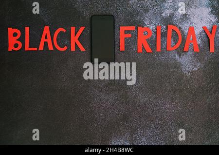 Black Friday Konzept. Inschrift 'Black friday', Laptop, Kaffeetasse, Mini-Warenkorb auf schwarzem Hintergrund. Platz zum Kopieren, Draufsicht, flach liegend. Kreativ Stockfoto
