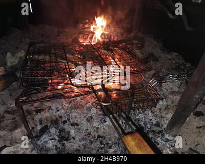 Fische in einem Grillständer auf Orangenfeuer und Holzkohle zu Grill. Stockfoto