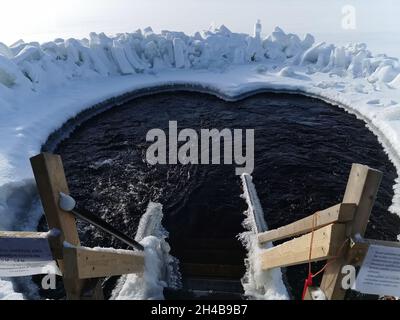 Gefrorene Holztreppen, die in ein Schneebad hinuntergehen. Eisbad stärkt den Körper gegen Kälte und Krankheiten. Eisschwimmen Stockfoto