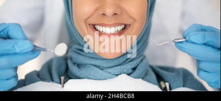 Zahnarztcheck. Nahaufnahme Der Lächelnden Muslimischen Lady, Die In Der Stomatologischen Klinik Behandelt Wird, Zahnarzt In Blauen Handschuhen, Die Zähne Der Islamischen Lady Besehen Stockfoto