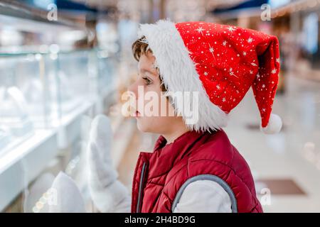 Boys in Santas Hut schaut durch das Fenster auf dem Markt in den Laden. Platz zum Kopieren, Platz für Text, Banner Stockfoto