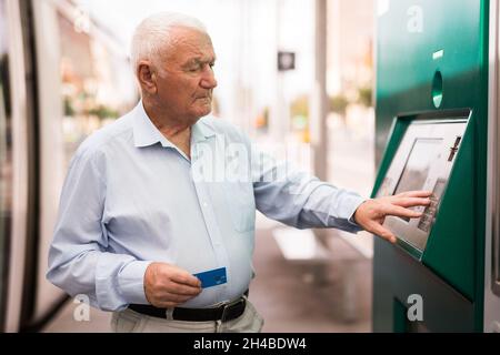 Alter Mann, der an der Straßenbahnhaltestelle einen Geldautomaten benutzte Stockfoto