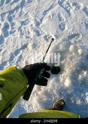 Hand in einer gelben dicken Jacke hält eine Angelrute auf Schnee. Stockfoto