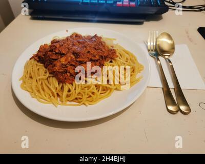 Spaghettis mit einer Sauce darauf vor einem Laptop und Besteck. Stockfoto