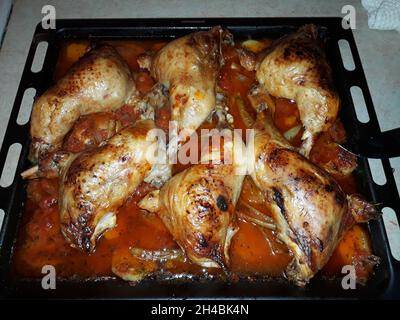 Hähnchenschenkel mit Gemüse und Tomatensauce in einem quadratischen schwarzen Backblech Stockfoto