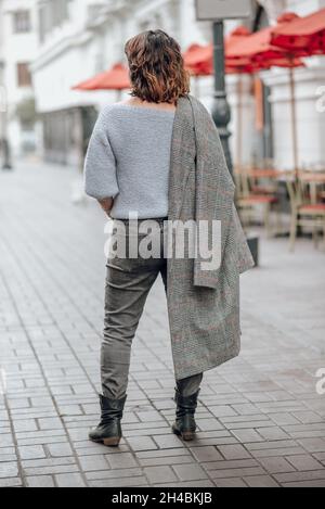 Rückseite einer Frau mit einem Sack in der Hand, Hintergrund mit roten Schirmen und Stühlen in einer niedlichen alten Straße Stockfoto