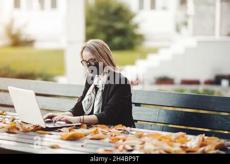 Frau, die draußen im Park an einem Laptop mit Gesichtsschutz arbeitet Stockfoto