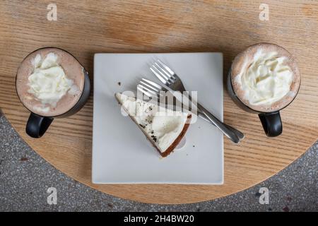 Zwei Tassen Mokka und eine Schokoladenkuchenscheibe auf einem Teller auf einem Holztisch Draufsicht Stockfoto