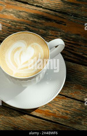 Weiße Tasse Cappucino auf dem rustikalen Holztisch. Draufsicht. Natürlicher Style. Vertikales Foto. Stockfoto