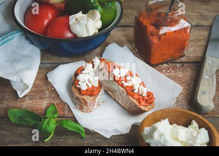 Vollkornbrot mit Tomaten-Pfeffer-Dip und Feta-Käse über alten rustikalen Holztisch bedeckt. Hausgemachtes Bio-Gemüsegericht. Stockfoto