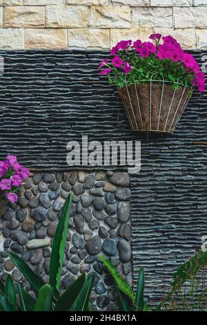 Die Wände sind mit grauen Steinen und Fliesen sowie hängenden Blumentöpfen verziert. Gartendekoration im Freien. Sommer Gartendekoration auf dem Hinterhof. Stockfoto