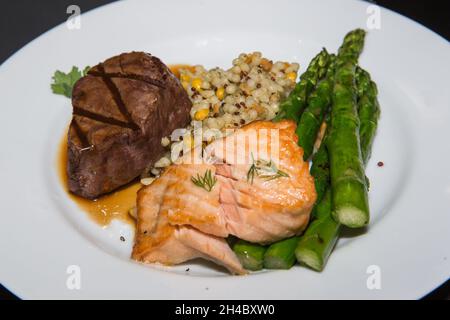 Ein Speiseteller mit Steak, gegrilltem Lachs, Kartoffelpüree und gebratenem Gemüse wird vorbereitet. Stockfoto