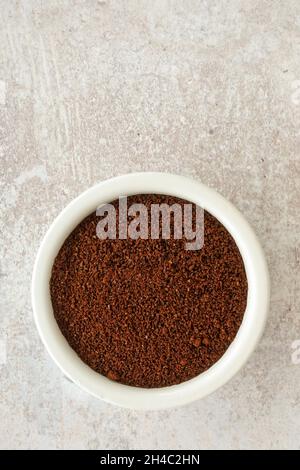 Gemahlene und geröstete Kaffeebohnen in einem weißen Keramikramekin auf Sandstein-Hintergrund mit viel Platz zum Kopieren. Draufsicht. Nahaufnahme. Stockfoto