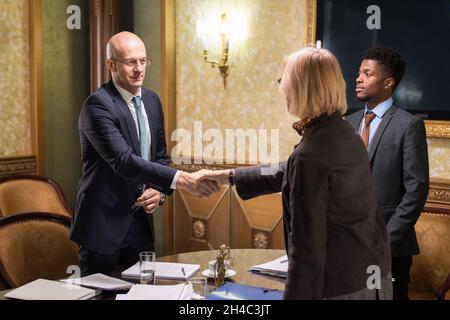 Zwei reife Geschäftspartner schütteln sich den Tisch mit Papieren, nachdem sie alle notwendigen Dokumente für die weitere Zusammenarbeit unterzeichnet haben Stockfoto