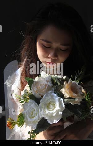 Nette vietnamesische Dame in einem weißen Kleid mit einem Blumenstrauß Stockfoto