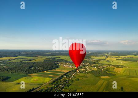 Roter herzförmiger Ballon mit Menschen über grünen Feldern und Wäldern. Stockfoto