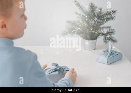 Weihnachten und Zero Waste, umweltfreundliche Verpackung. Eine Kinderhand in umweltfreundlichem, wiederverwendbarem Stoffpaket auf einem weißen Tisch. High qu Stockfoto