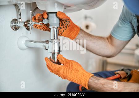 Männliche Klempnerhände zur Befestigung des Metallwaschrohrs Stockfoto