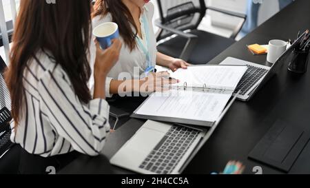 Beschnittenes Bild einer weiblichen Angestellter im Team einer Anwaltskanzlei, die auf Geschäftsvertragsdokumenten schaut und spricht. Stockfoto