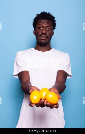 afroamerikanische Person, die Zitronen hält und posiert. Schwarzer Mann zeigt Cirtus-Früchte zur Kamera für einen gesunden Lebensstil. afroamerikanischer Erwachsener mit gelbem Snack für saftige, Vitamine und Ernährung Stockfoto