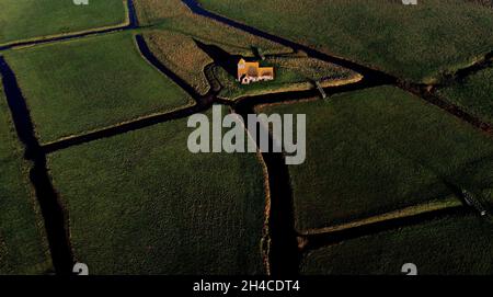 Blick auf die St. Thomas Becket Kirche während der Morgensonne in Fairfield bei Ashford. Das kleine Gebäude stammt aus dem späten 12. Jahrhundert und liegt isoliert auf einem Feld, das von Deichen durchtrennt und von Schafen auf dem Romney Marsh in Kent beweidet wurde. Bilddatum: Dienstag, 2. November 2021. Stockfoto