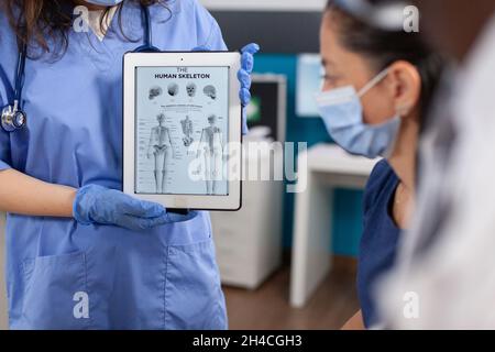 Kinderarzt hält einen Tablet-Computer mit Knochenradiographie auf dem Bildschirm mit Schutzhandschuhen gegen Kovid19. afroamerikanischer Arzt erklärt medizinische Expertise im Krankenhausbüro Stockfoto