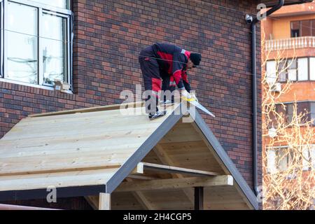 Krasnodar, Russland - 17. Dezember 2020: Ein Dachdecker mit einer Säge in den Händen baut ein Dach Stockfoto