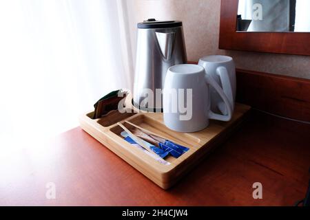 Willkommenstablett mit Wasserkocher, Tassen, Tee und Zucker auf dem Tisch vor dem Fenster im Hotel Stockfoto