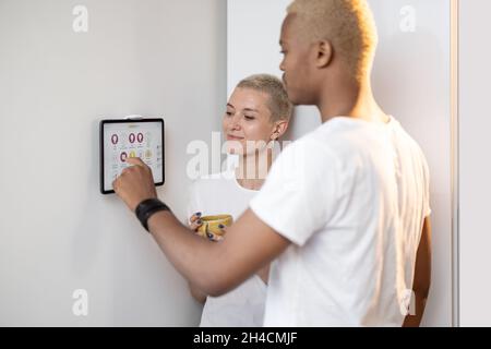 Junges Paar, das Smart-Home-Geräte auf einem digitalen Tablet steuert Stockfoto
