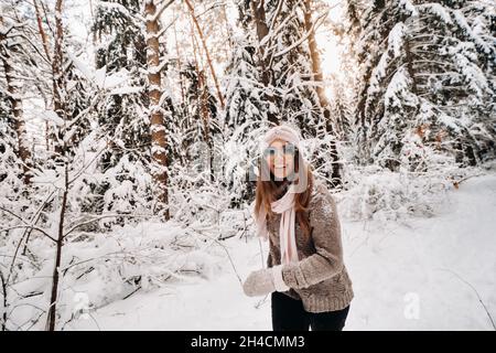 Ein Mädchen mit Pullover und Brille geht im Winter durch den verschneiten Wald.