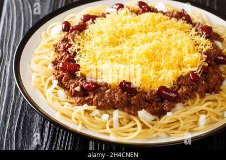 Hausgemachte Cincinnati Chilli Spaghetti mit rotem Bohnen-Käse und Zwiebel aus nächster Nähe auf dem Teller auf dem schwarzen Holzhintergrund. Horizontal Stockfoto