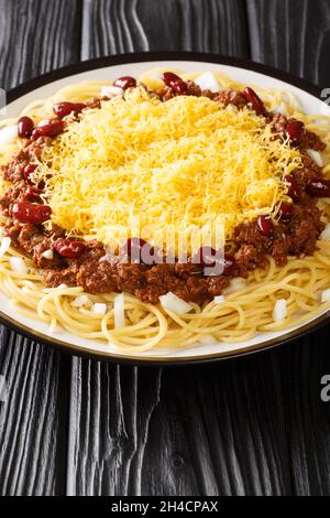 Authentic Cincinnati Chili ist ein fleischiges, reiches und einzigartig gewürztes Chili, das über heiße Spaghetti mit Käseauflagen in der Nähe auf dem Blac-Teller serviert wird Stockfoto