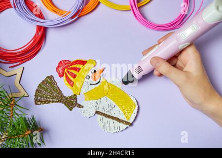 Ein Mädchen zeichnet einen Schneemann mit einem 3d-Stift auf einem violetten Hintergrund Stockfoto